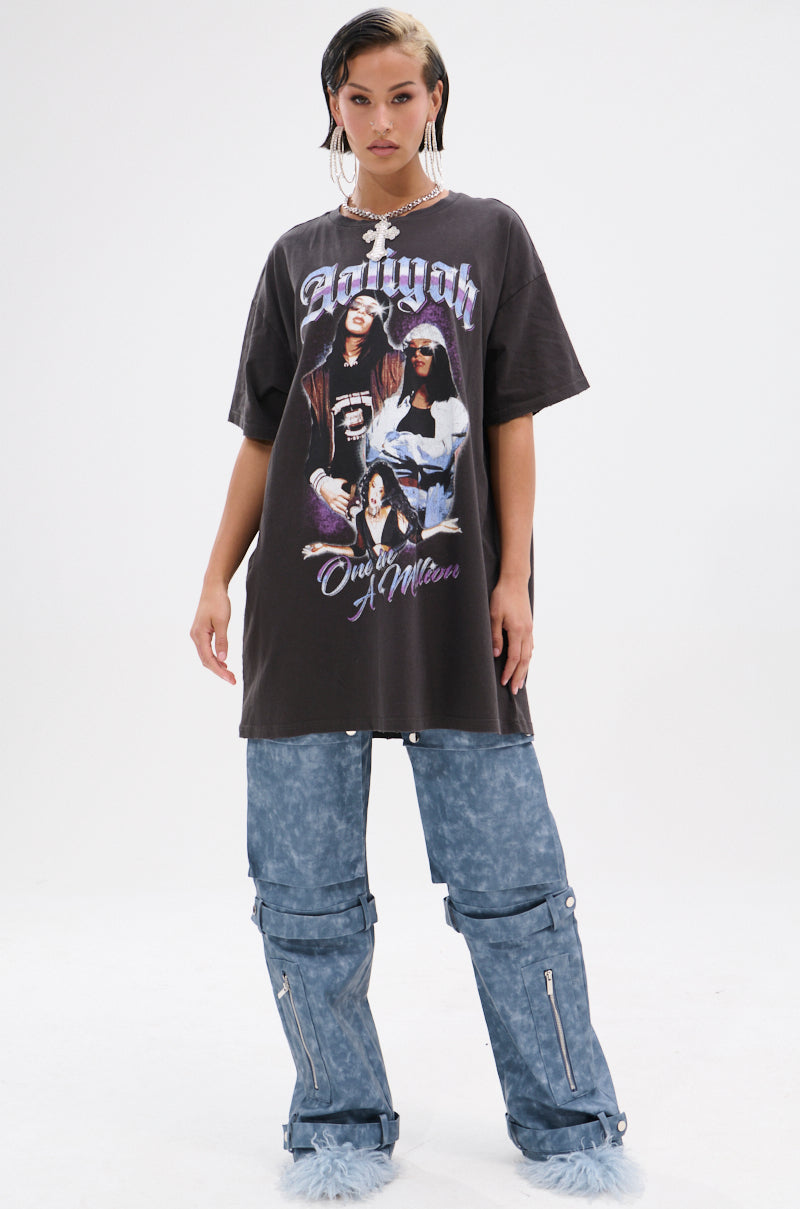 A young woman poses against a white background in the AALIYAH FOREVER GRAPHIC TSHIRT DRESS, styled with blue-gray baggy zippered pants, fur-tipped shoes, hoop earrings, and a chunky chain for an iconic tribute look.