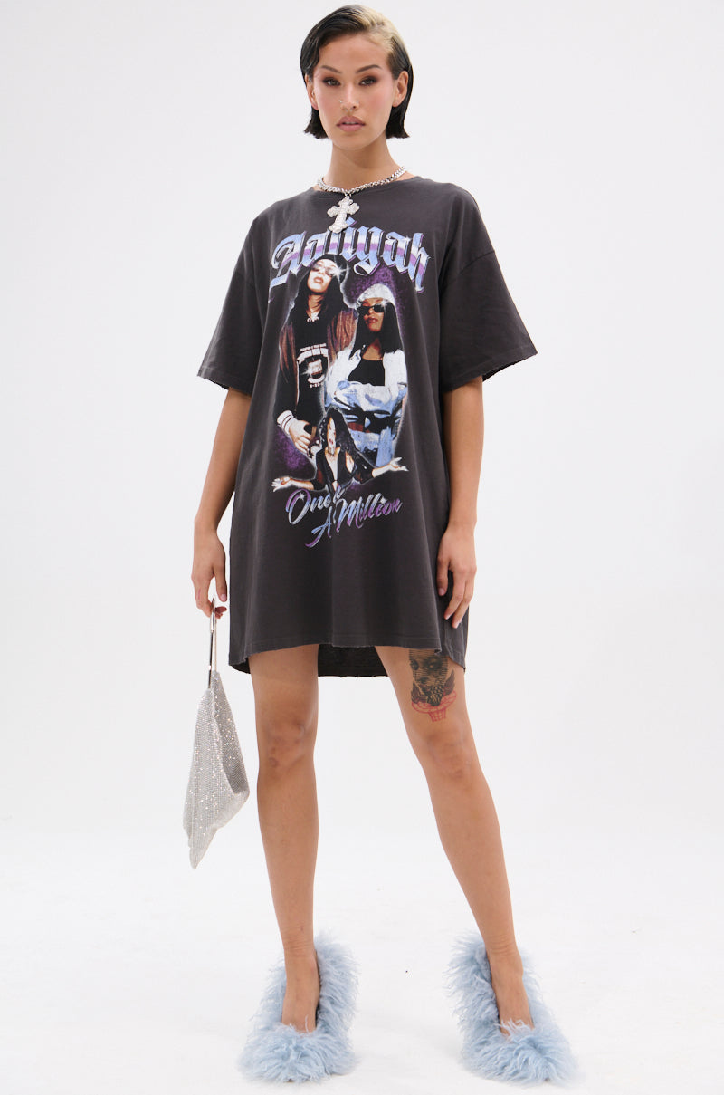 A woman with a short hairstyle and leg tattoos stands against a white background wearing the AALIYAH FOREVER GRAPHIC TSHIRT DRESS, paired with a sparkly silver handbag and fluffy blue slippers.