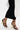 A person in black and white clothing walks in the AZALEA WANG AYYAR BLACK GOLD WEDGE HEEL SANDAL, featuring unique gold accents, against a white background.