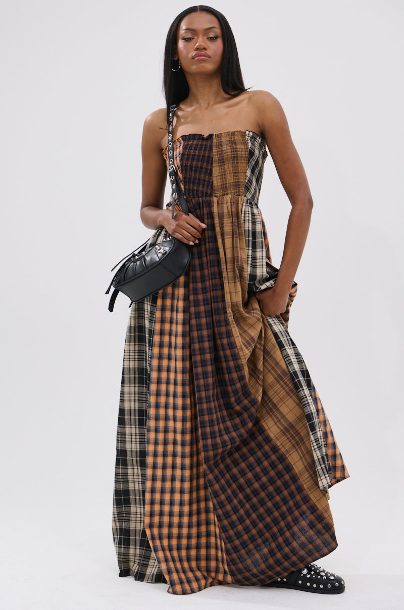 A woman poses against a white backdrop in the FALL IN LOVE PLAID MAXI DRESS, featuring 90’s-inspired brown and black plaid, styled with a black crossbody bag and studded shoes for edgy punk princess vibes.