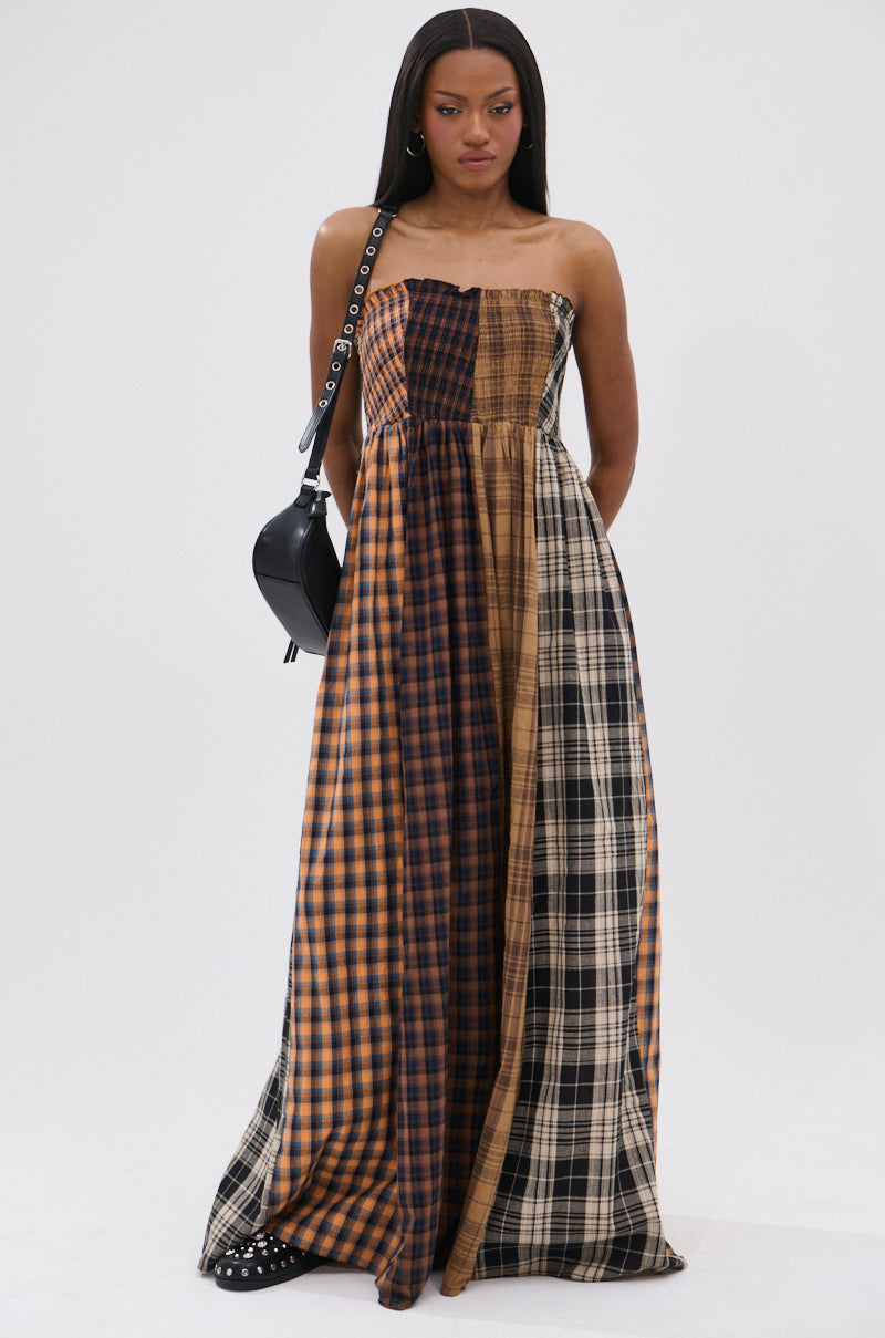 A woman channels punk princess style in the FALL IN LOVE PLAID MAXI DRESS—a strapless, patchwork plaid maxi in brown, orange, and black—paired with a black shoulder bag and studded shoes against a plain white background.
