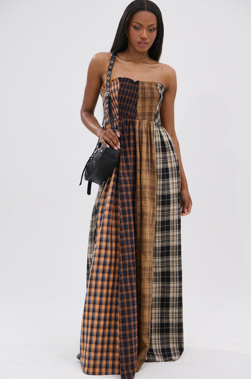 A woman stands against a plain white background wearing the FALL IN LOVE PLAID MAXI DRESS, featuring mixed brown and black plaid patterns, and holds a black crossbody bag.