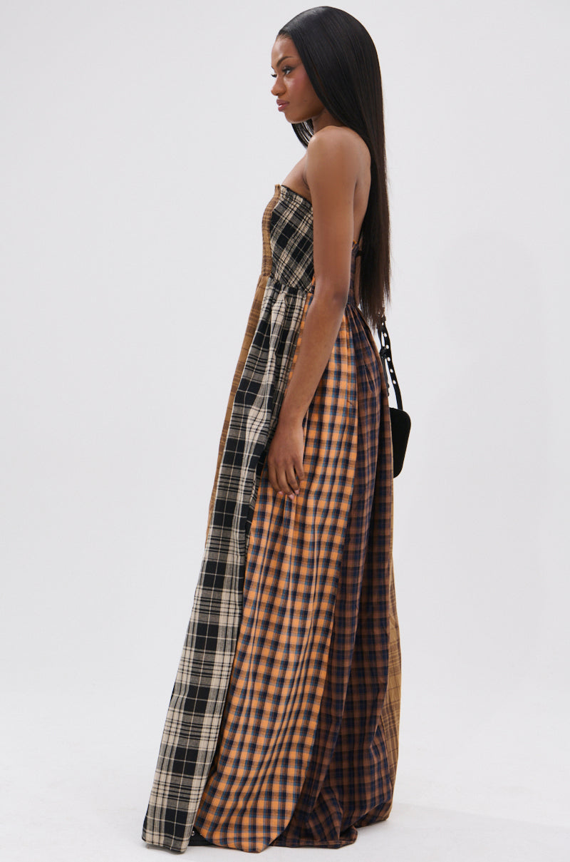 A woman in profile channels 90’s punk princess style in the FALL IN LOVE PLAID MAXI DRESS, featuring black, brown, and tan panels. Her straight hair and a small black bag complete the edgy ensemble.