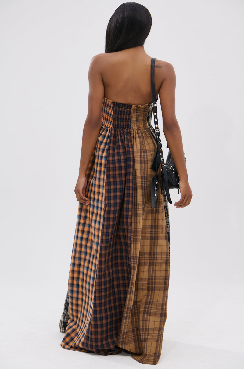 A woman channels effortless cool in the FALL IN LOVE PLAID MAXI DRESS, featuring brown and black plaid. With long straight hair and a black handbag over her shoulder, she stands with her back to the camera in 90’s-inspired style.