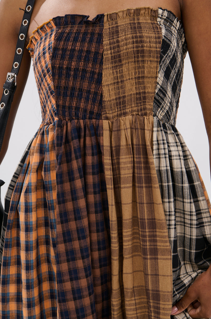 A close-up of a person in the FALL IN LOVE PLAID MAXI DRESS, a strapless maxi with mixed brown, black, and cream plaid patterns, gathered fabric, a black shoulder strap, and 90’s-inspired punk princess vibes.