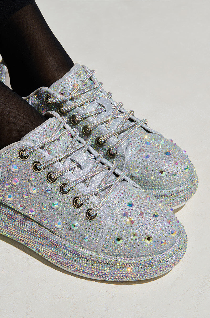The AZALEA WANG AZURE SILVER RHINESTONE SNEAKER, adorned with rhinestones and thick black laces, pairs perfectly with black tights against a light backdrop.