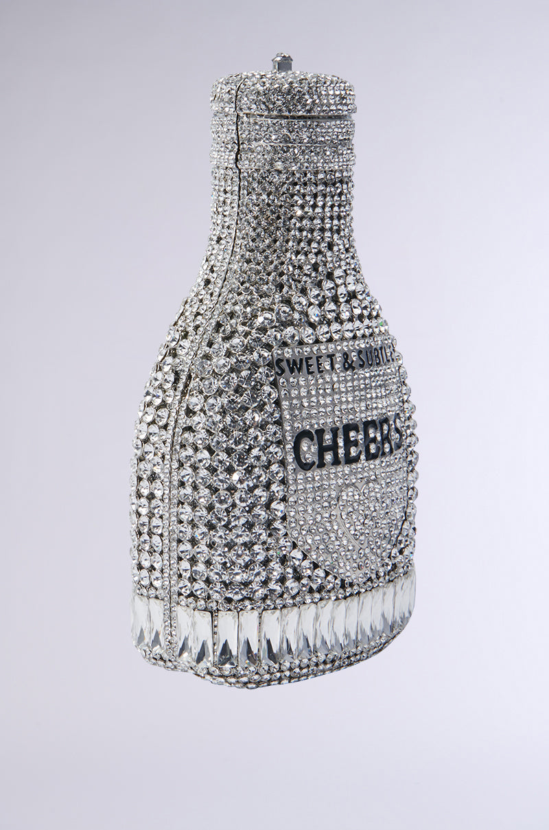 The CHEERS BLING PURSE is a bottle-shaped novelty handbag embellished with silver and clear crystals. It features the words "CHEERS" and "SWEET & SUBTLE," exuding luxury through its intricate detailing and geometric pattern at the bottom, making it truly sparkling. 2