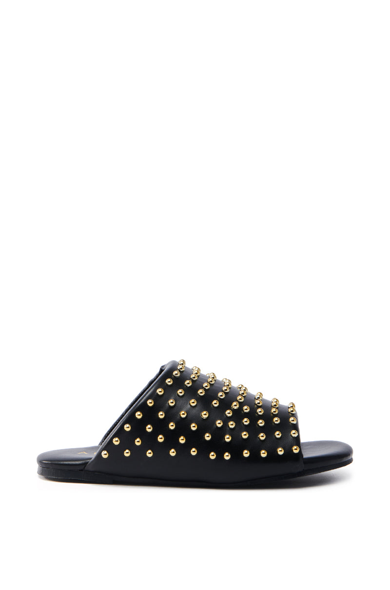 The AKIRA BAGGER Studded Slip-On Sandal in black features a flat sole and faux leather design adorned with rows of gold studs, elegantly presented against a white backdrop.