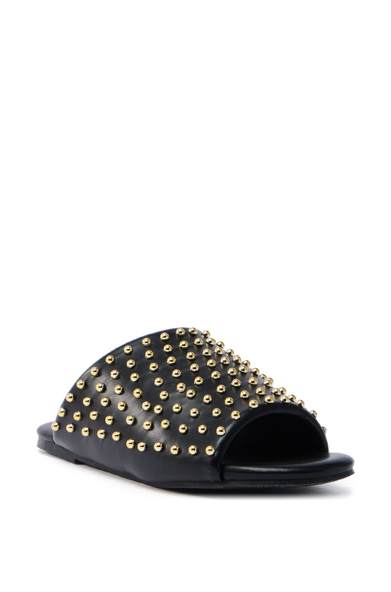 The AKIRA BAGGER STUDDED SLIP ON SANDAL in black features gold stud embellishments on sleek faux leather straps. The footbed is flat for comfort, and the studs add a fashionable edge.