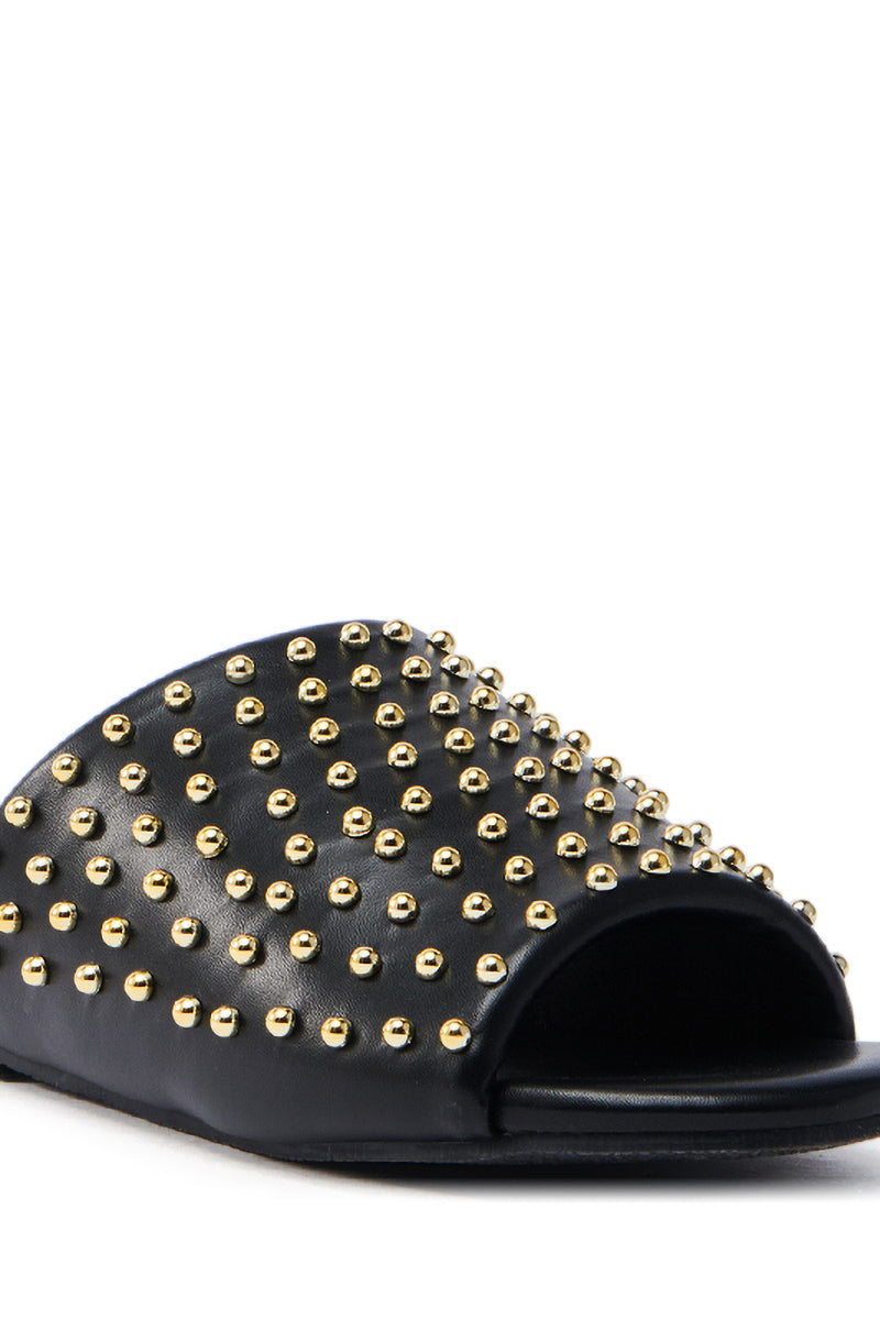 The AKIRA BAGGER STUDDED SLIP ON SANDAL IN BLACK is a black faux leather sandal with an open-toe design, flat sole, and adorned with small gold studs.