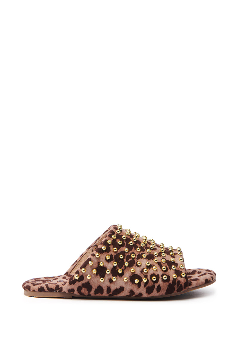 The AKIRA BAGGER Studded Slip-On Sandal in Leopard features a flat rubber sole, a soft fabric strap adorned with gold studs, and embodies the essence of a studded slip-on.
