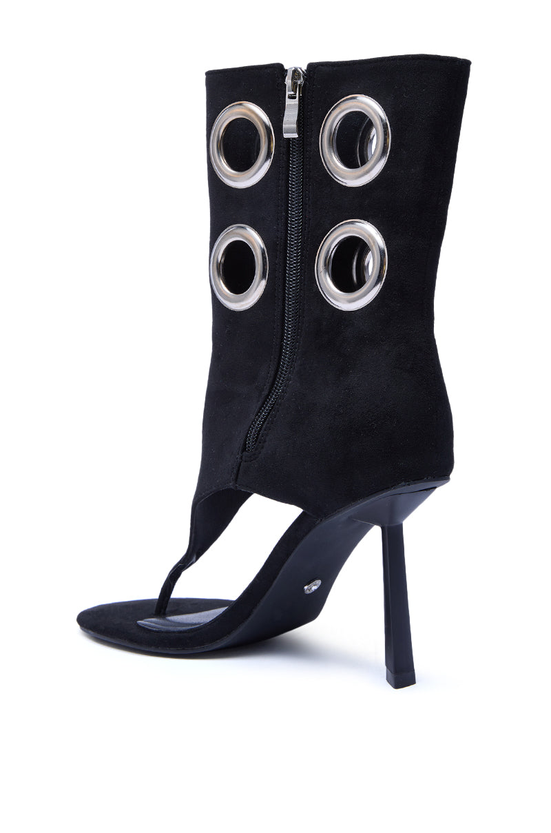 The AZALEA WANG BAINA BLACK GROMMET DETAIL GLADIATOR SANDAL is a striking, mid-calf black boot with stiletto heel, side zipper, open toe, and four metallic grommets for a chic modern look.