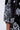 Close-up of a person's arm in the BOUJEE BANDANA SEQUIN MINI DRESS IN BLACK, showcasing intricate white sequin and floral patterns on an elbow-length sleeve, set against a plain, light-colored background.
