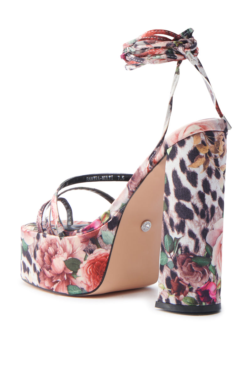 The AZALEA WANG BANIRA MULTI CHEETAH FLORAL CHUNKY SANDAL flaunts a satin upper in vibrant floral and leopard prints. It boasts an ankle strap, sturdy heel, and diamond-shaped embellishments on the sole against a plain white backdrop.