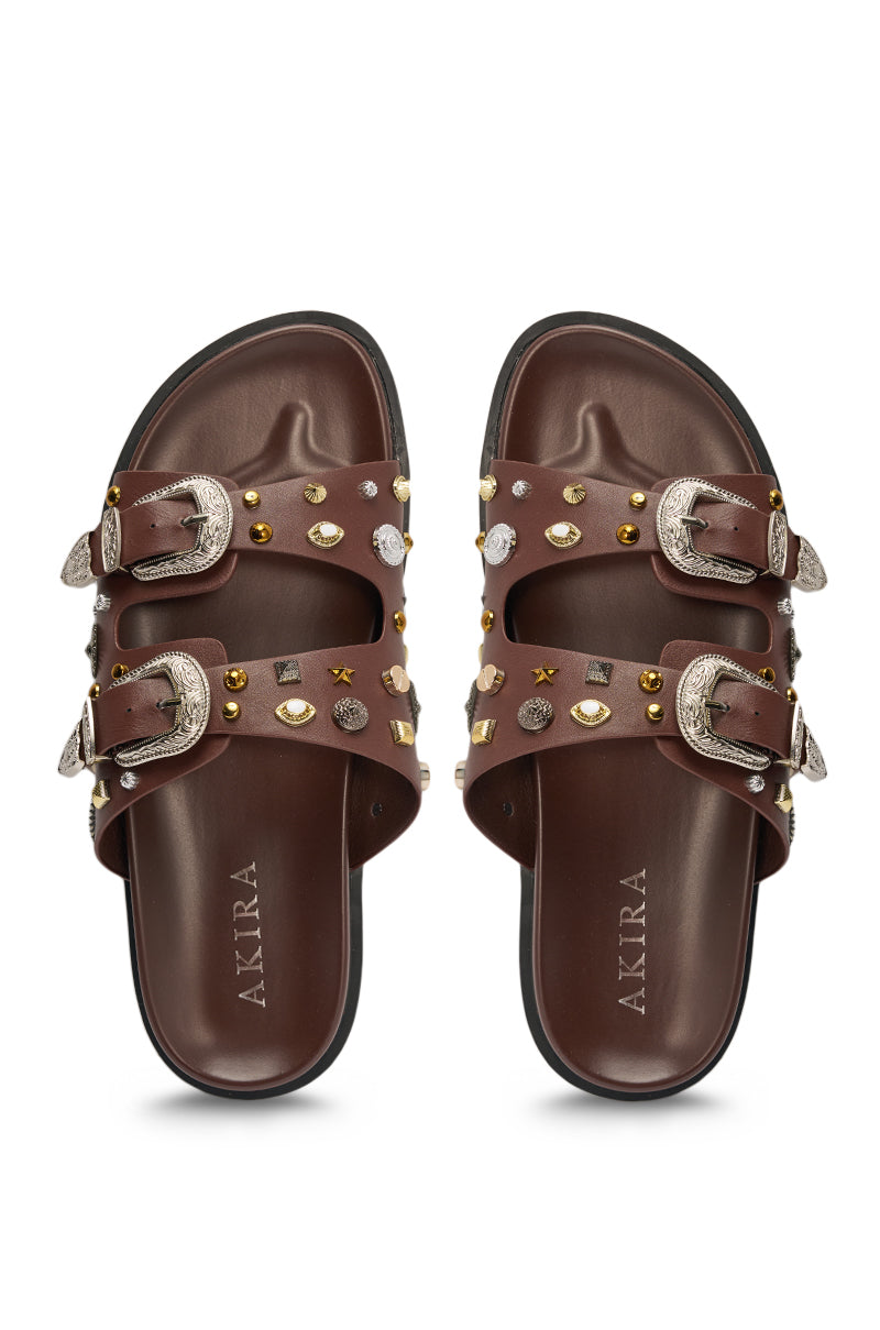The AKIRA BARCLAY Brown Metal Embellished Slip On Flat Sandal features silver buckles, gold and silver stud strap embellishments, and contoured footbeds branded with "AKIRA. 3