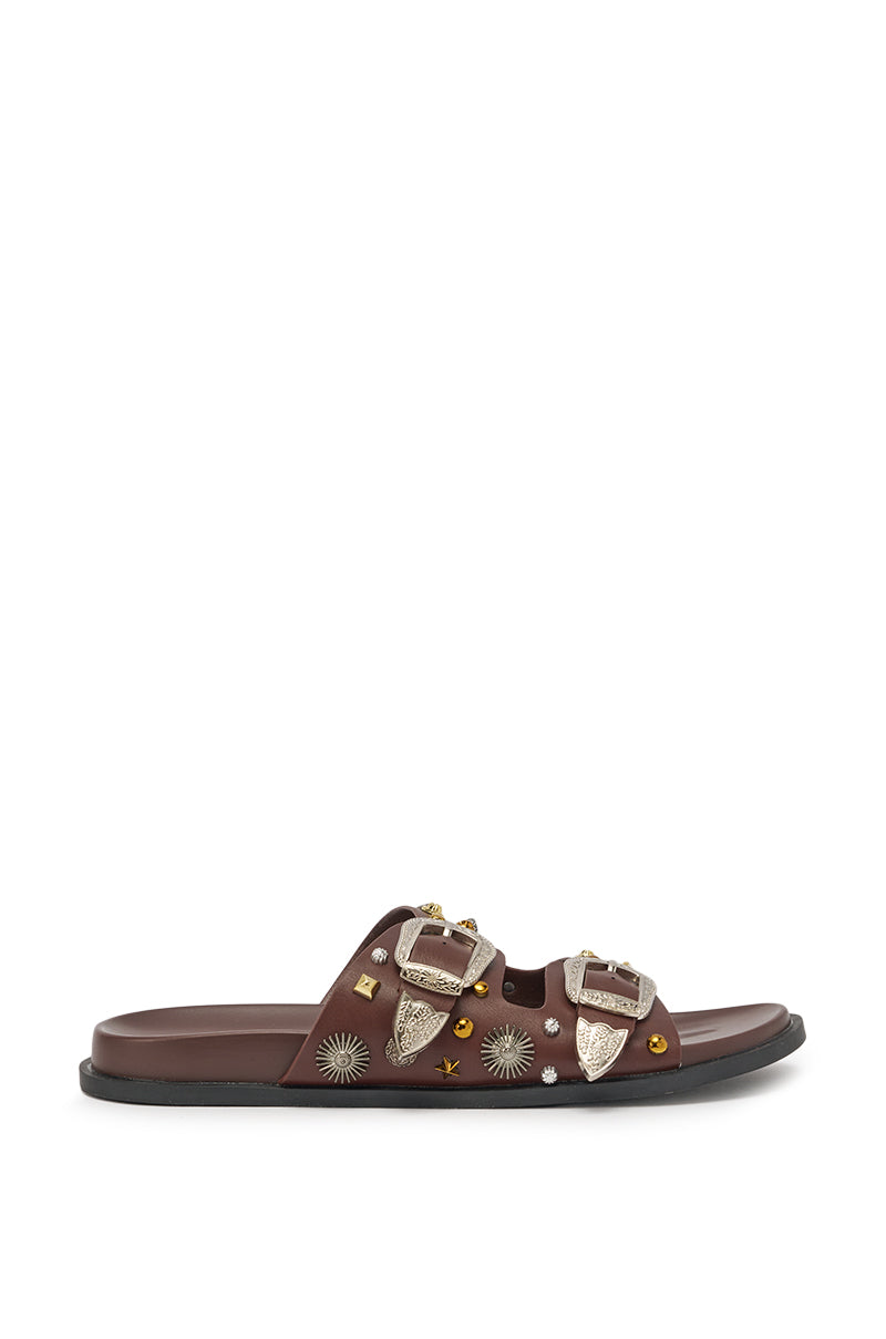 The AKIRA BARCLAY BROWN METAL EMBELLISHED SLIP ON FLAT SANDAL features two silver buckles, metallic sun and star accents on a brown faux leather upper, and a flat black sole. 4