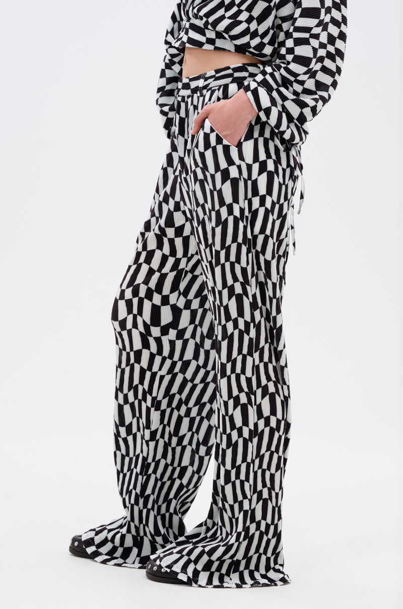 A person stands against a plain white background with one hand in their pocket, wearing loose BARI CHECKERED TROUSER in black and white, paired with a matching long-sleeve top.