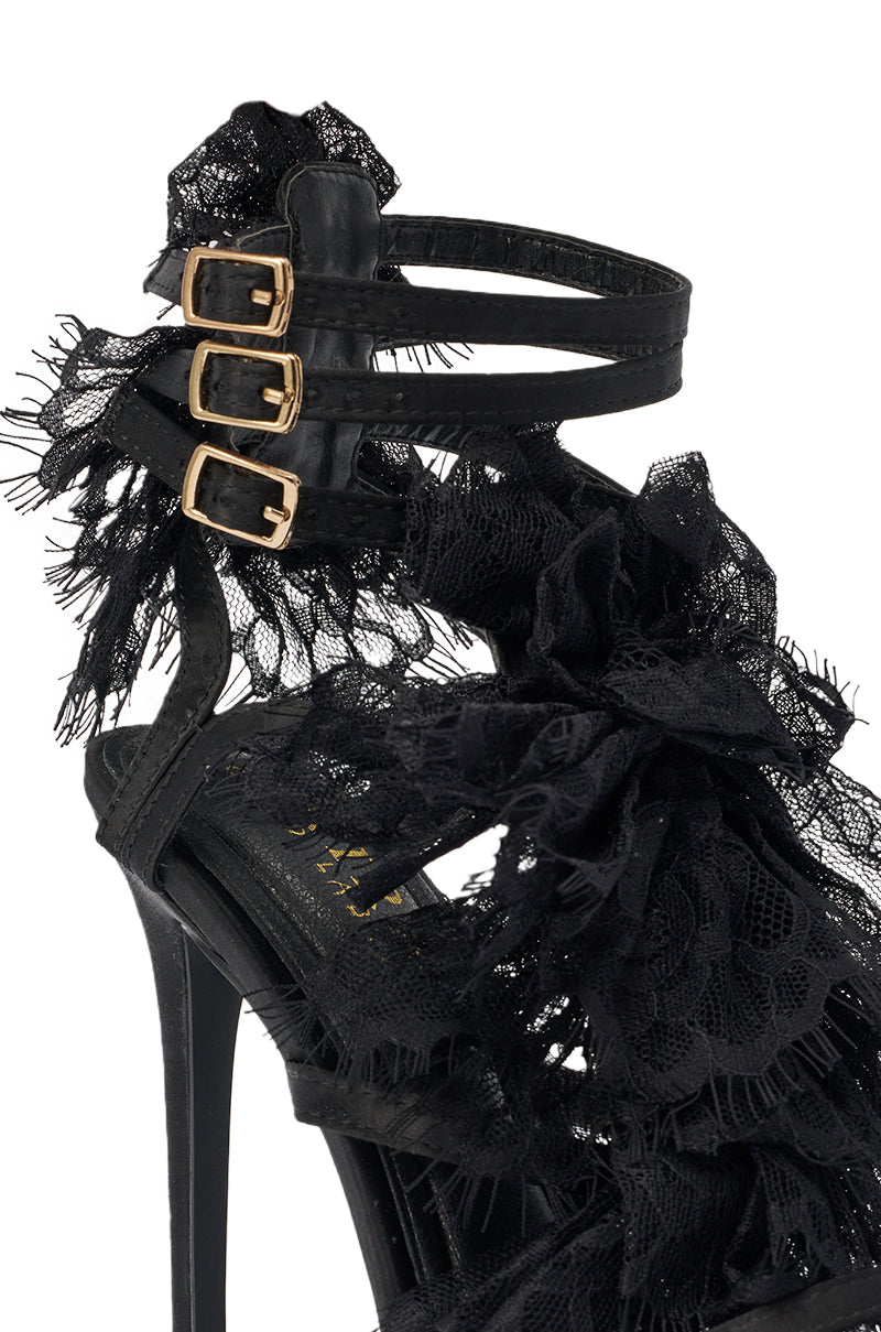 A close-up of the AKIRA GOLD BARRISTER BLACK LACE DETAIL STILETTO SANDAL, showcasing black stiletto heels with detailed black lace ruffles and three gold ankle buckles for an elegant, intricate look. 6