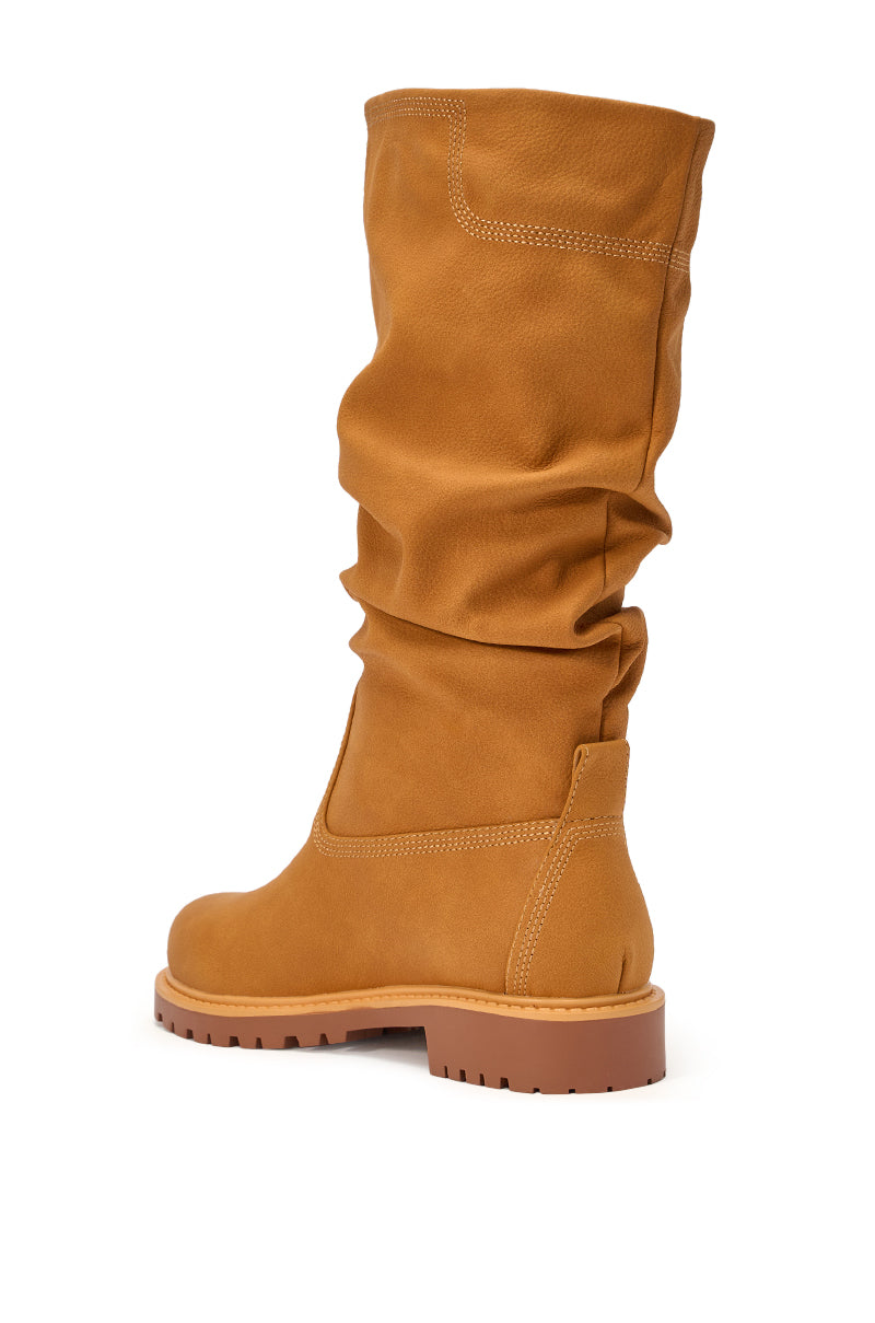 The AKIRA GOLD BARTLETT TAN FLAT RUCHED BOOTIE features tan faux leather, a ruched shaft, chunky treaded sole, visible stitching, and a relaxed casual style, shown angled from the back and side. 6