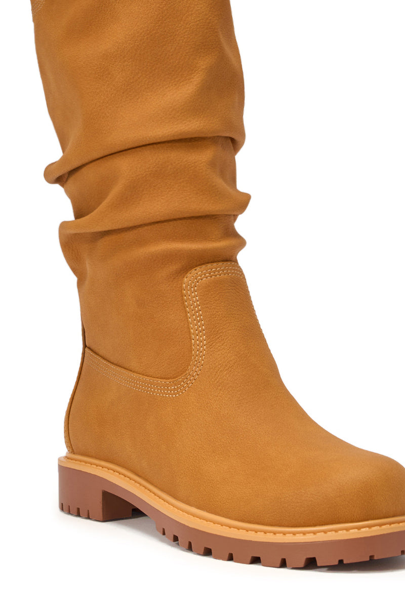 Close-up of the AKIRA GOLD BARTLETT TAN FLAT RUCHED BOOTIE featuring a tan ruched shaft, visible stitching, rounded toe, and light brown rubber lug sole against a white background. 7