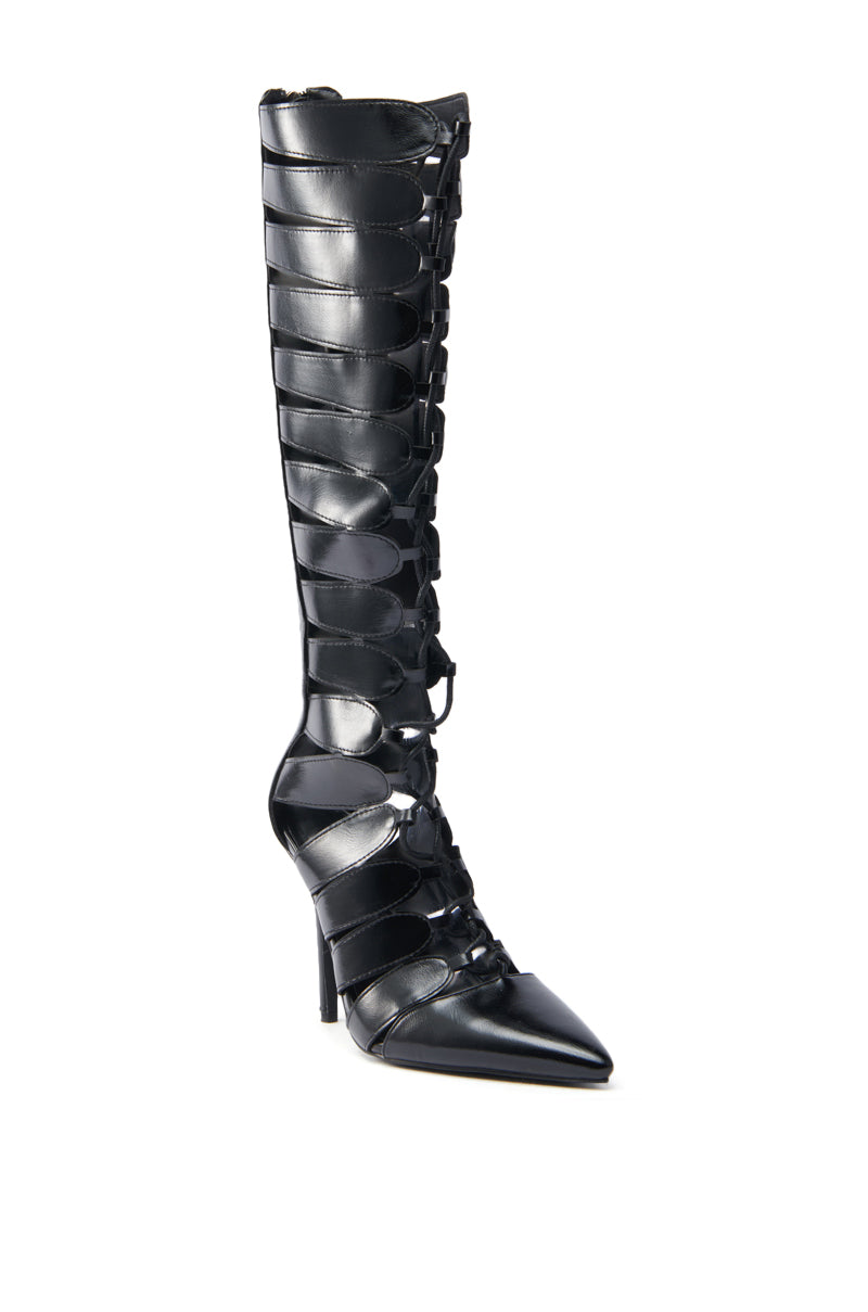 The AZALEA WANG BASTIAN BLACK BOOT is a high stiletto boot in vegan leather with z-shaped cutouts, a pointed toe, and intricate front lace-up detailing, blending elegance with modern style.