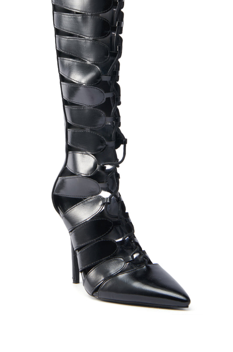 The AZALEA WANG BASTIAN BLACK BOOT is a knee-high vegan leather boot with pointed toes, stiletto heels, intricate lace-up detailing, wide straps, and stylish cut-outs along the front.