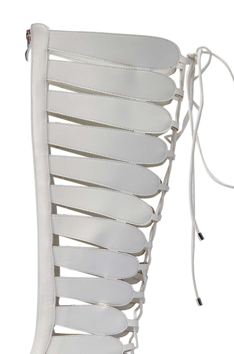 Close-up of the AZALEA WANG BASTIAN WHITE BOOT, a knee-high gladiator in luxe faux leather, featuring multiple horizontal straps, lace-up side detail, stiletto heel, open strap design, and top zipper.