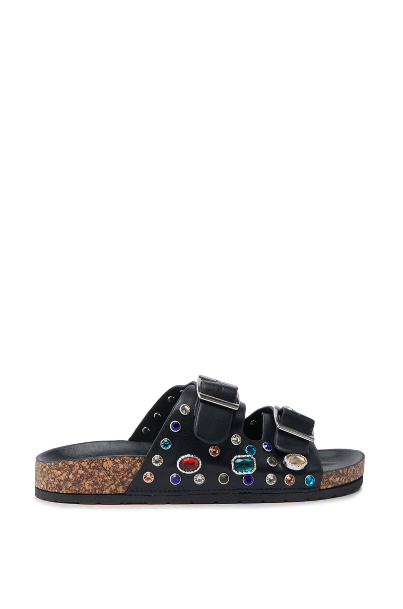 The AKIRA BAYLEAVES SLIP ON BLACK SANDAL features black faux leather, two straps with large metal buckles, a cork sole, and vibrant gemstone accents highlighted by metal studs on the upper.