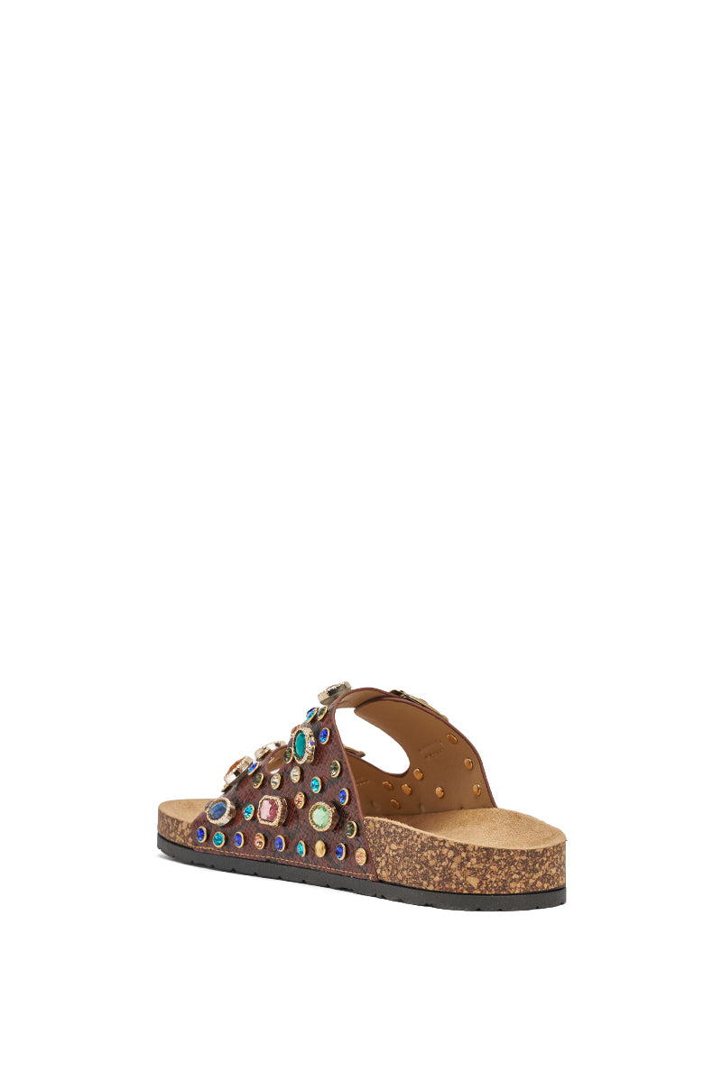 The AKIRA BAYLEAVES Brown Snake Embellished Flat Slip-On Sandal features brown faux leather with a cork sole and colorful gemstone/stud accents on the strap, displayed from a rear side angle against a white background. 8