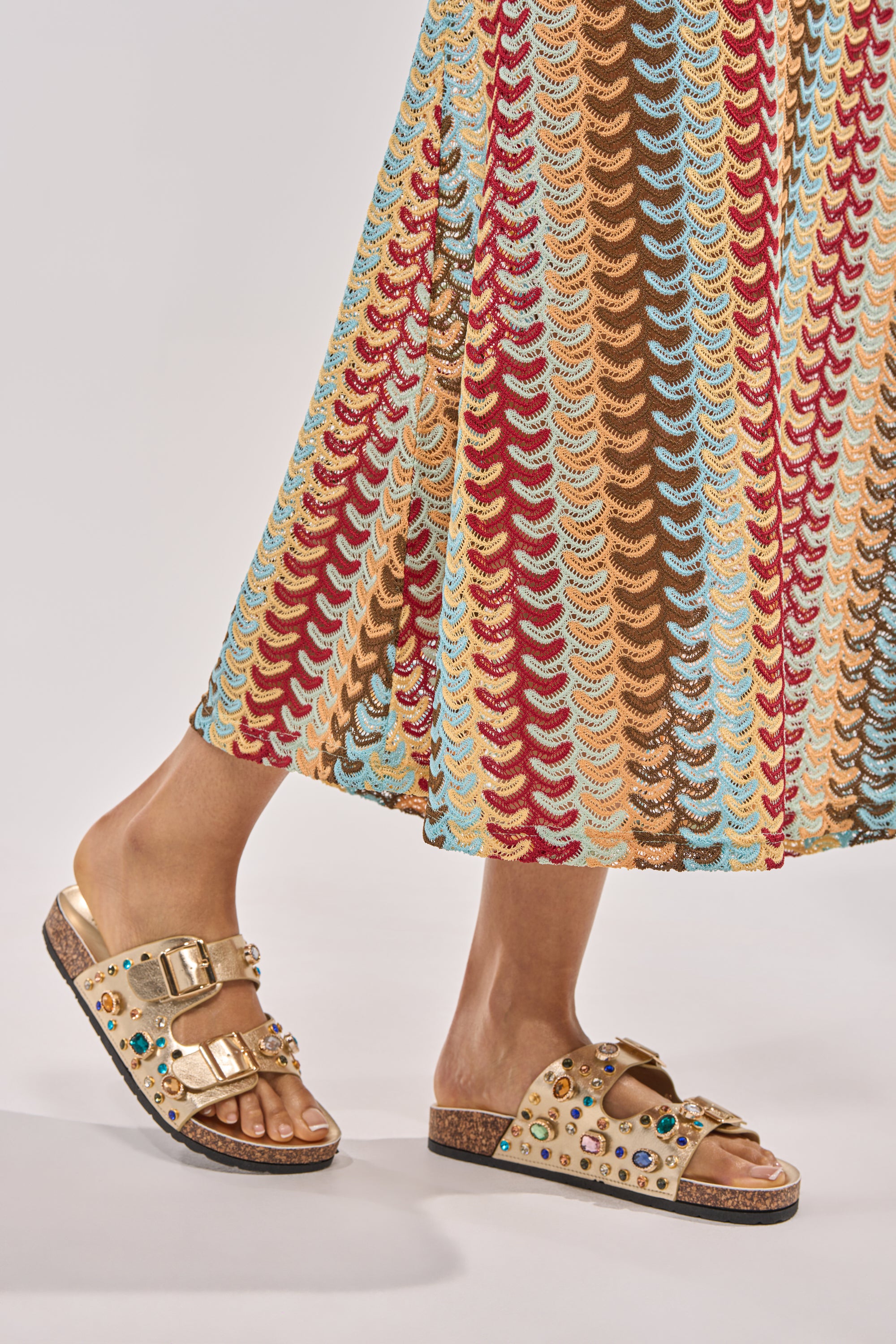 Wearing a long, colorful zigzag skirt, the person stands on a light background with their AZALEA WANG BAYLEAVES GOLD EMBELLISHED SANDAL sparkling under the light. 3