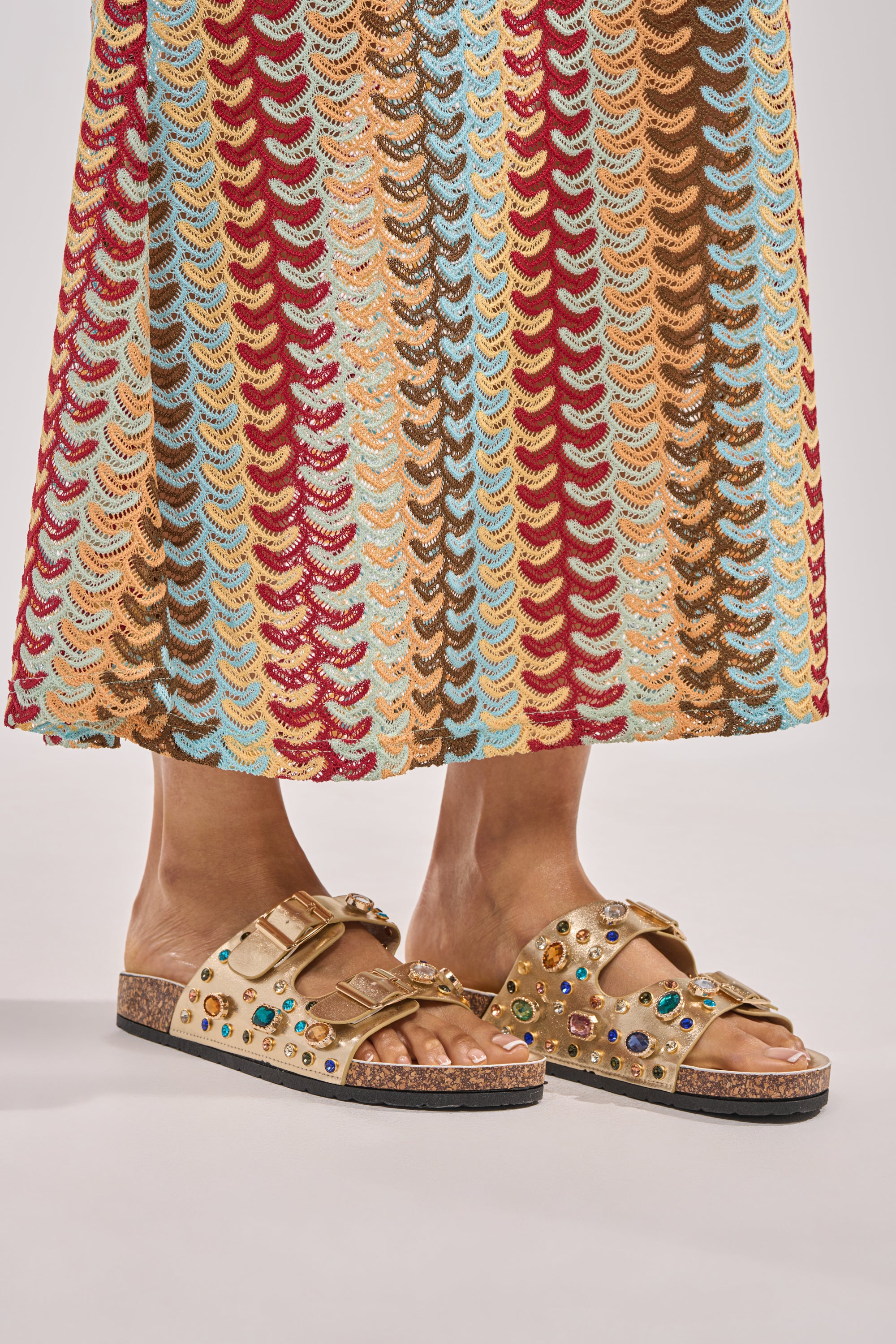A person wears a colorful crocheted skirt and the AZALEA WANG BAYLEAVES GOLD EMBELLISHED SANDAL, standing on a neutral background. 9