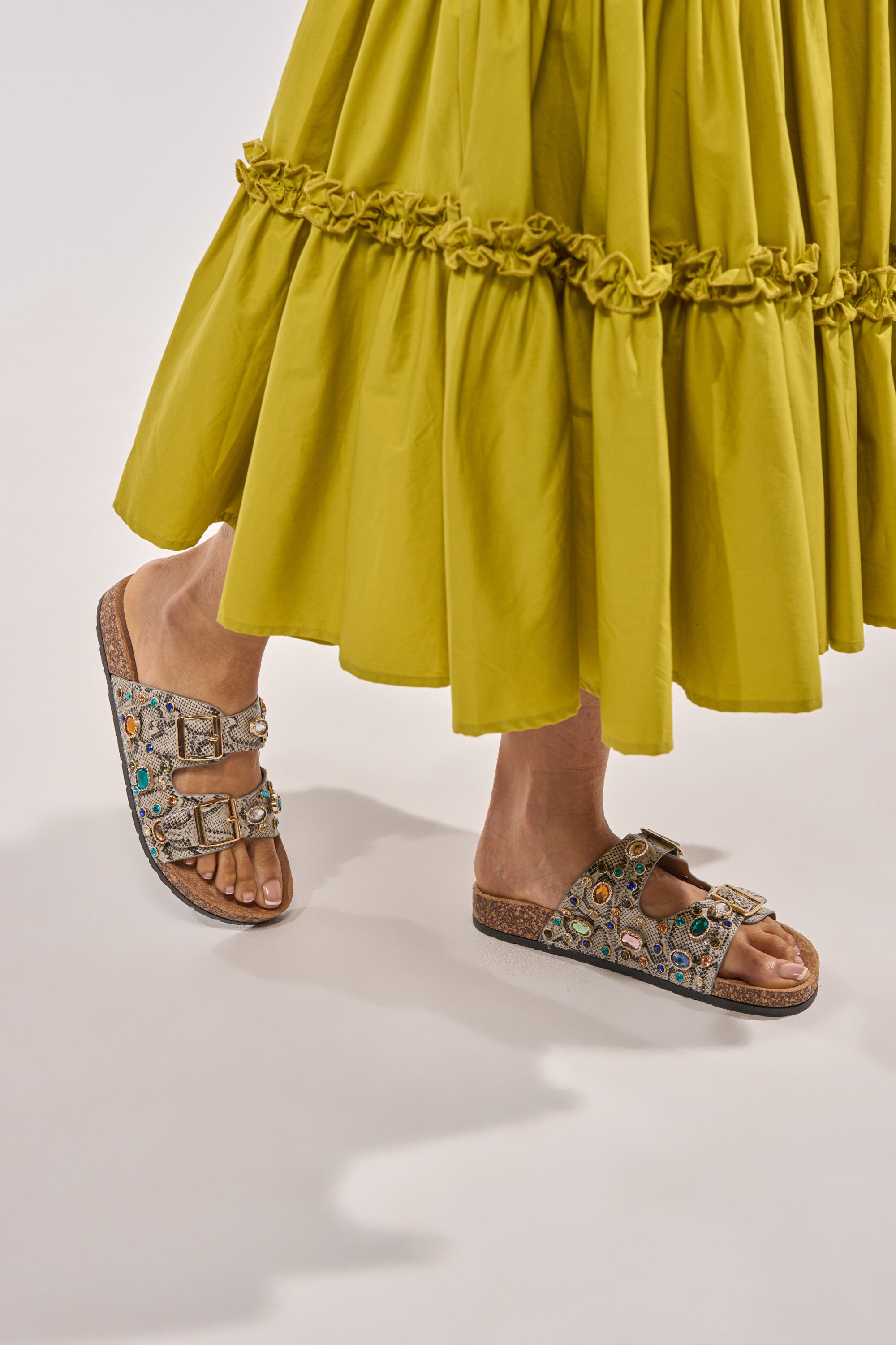 A person in an olive green ruffled skirt wears AKIRA BAYLEAVES SNAKE EMBELLISHED FLAT SLIP ON SANDALS, standing on a light background. 0
