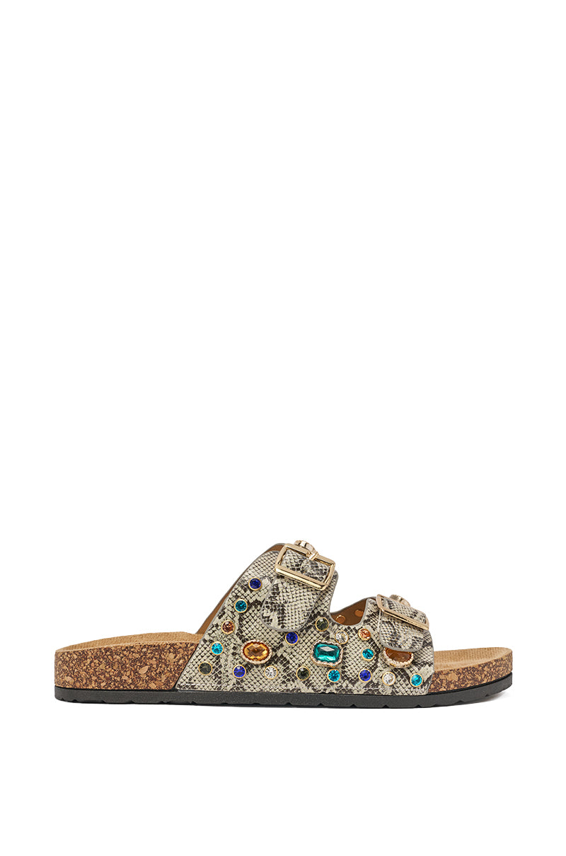 The AKIRA BAYLEAVES SNAKE EMBELLISHED FLAT SLIP ON SANDAL features textured beige faux leather straps with colorful gem-like accents and gold buckles, set on a cork sole and shown in a side view against a white background. 3