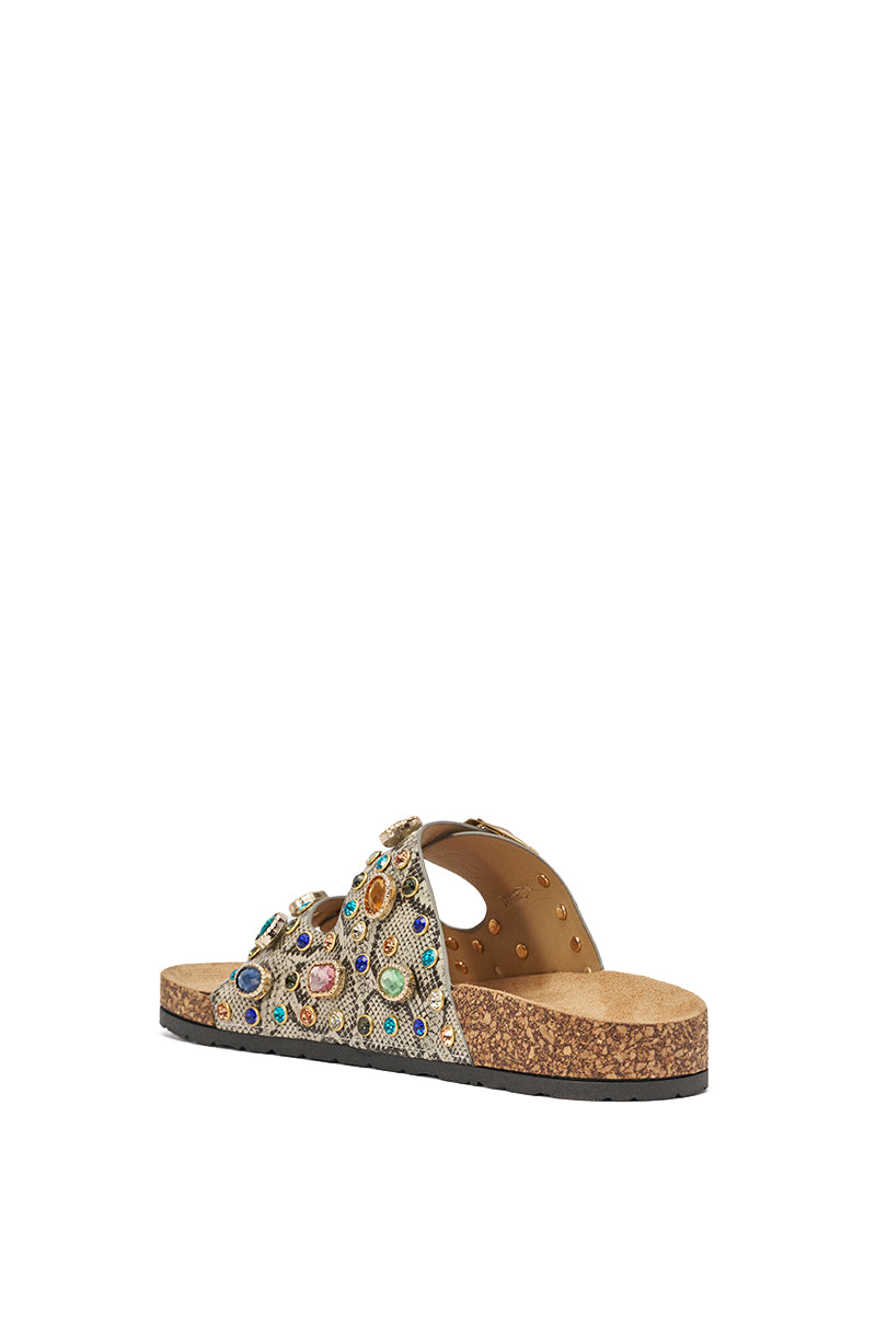 The AKIRA BAYLEAVES SNAKE EMBELLISHED FLAT SLIP ON SANDAL features a cork sole, black bottom, and textured beige straps with colorful gemstone-like accents, shown from a slight rear angle on a white background. 5