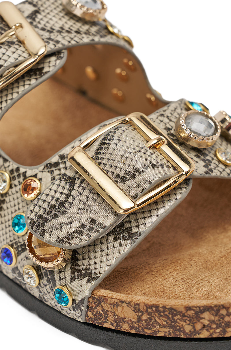 The AKIRA BAYLEAVES SNAKE EMBELLISHED FLAT SLIP ON SANDAL features rhinestones, a chic snakeskin pattern, gold buckles, colorful jewel accents, faux leather straps, a comfy cork footbed, and a black sole. 6