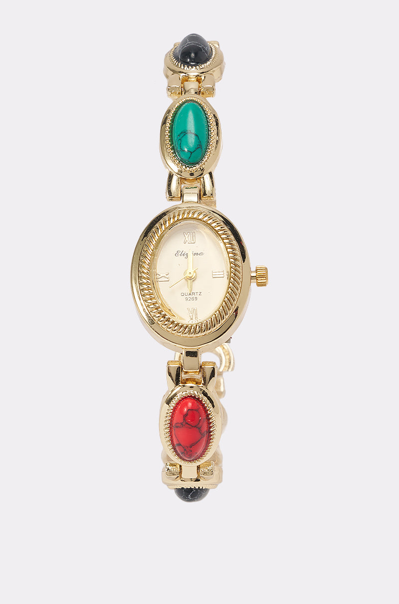 Introducing the JEWELS FOR EVERYONE WATCH—a stunning gold-tone timepiece featuring a round marbled stone face with Roman numerals and the word "Quartz." Its elegant band is adorned with oval gemstones in green, red, and black, making this unique watch the perfect accessory for any occasion.