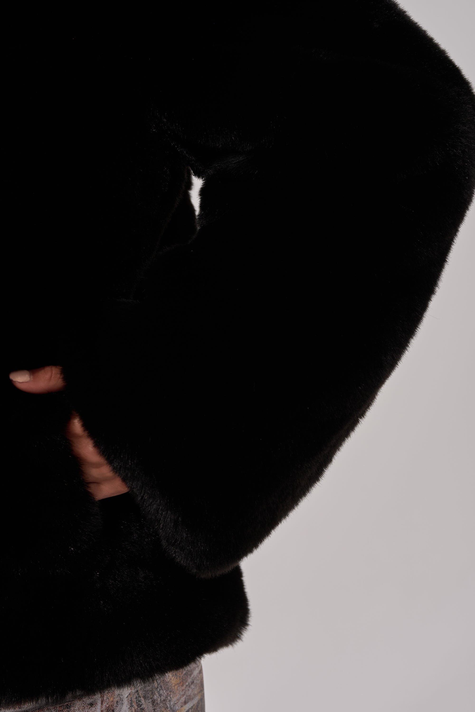 Model showcases the NO LOOKING BACK FAUX FUR IN BLACK, standing with one hand on their hip to display both the luxurious texture of the oversized black faux fur coat and its stylish silhouette against a plain light background.