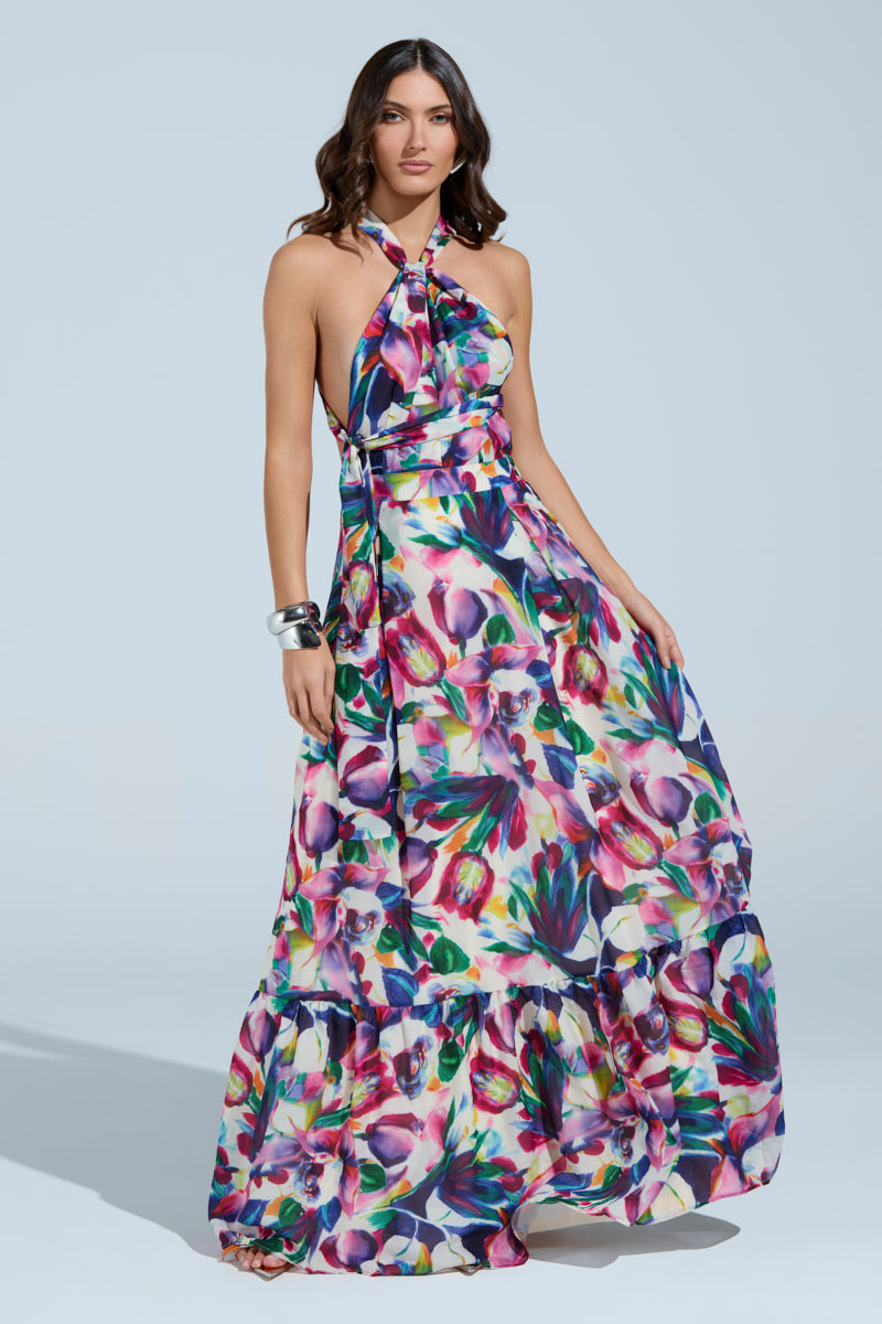 In a lively setting, she dons the BETTER BE MAXI DRESS with its vibrant floral pattern and halter neckline. Her wavy hair flows gently, complemented by silver bangles, creating a relaxed yet confident aura.