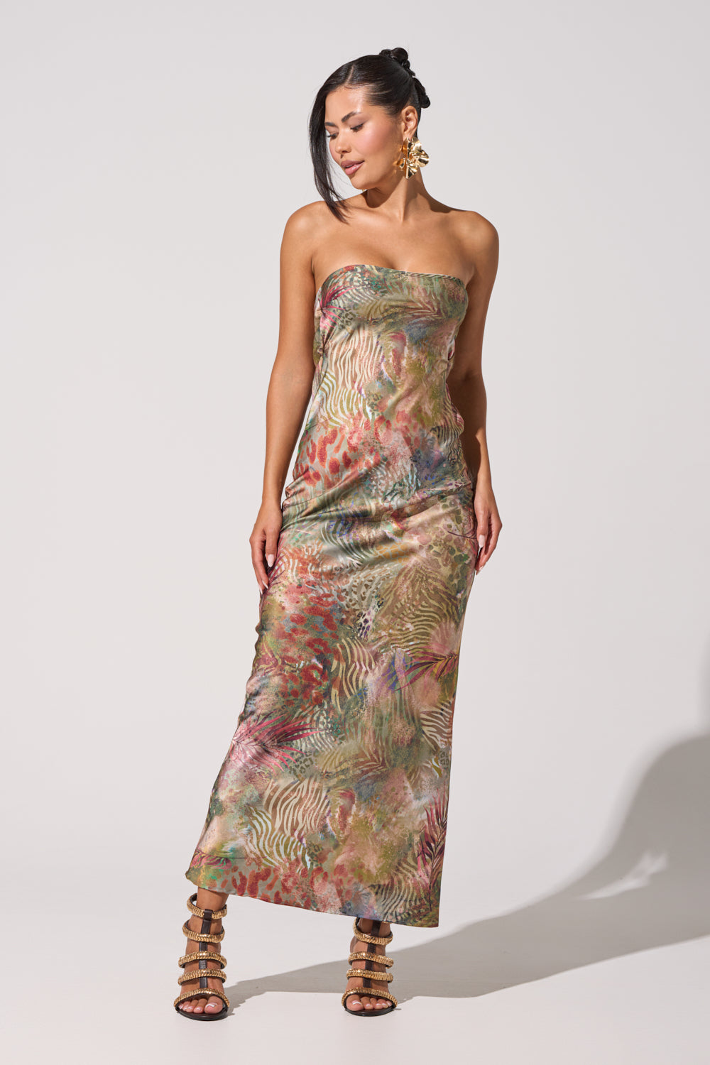 A woman models the IT GIRL SATIN MAXI DRESS, a vibrant strapless maxi with mixed animal print, against a white background. She pairs it with statement earrings, strappy high-heeled sandals, and wears her dark hair down. 2
