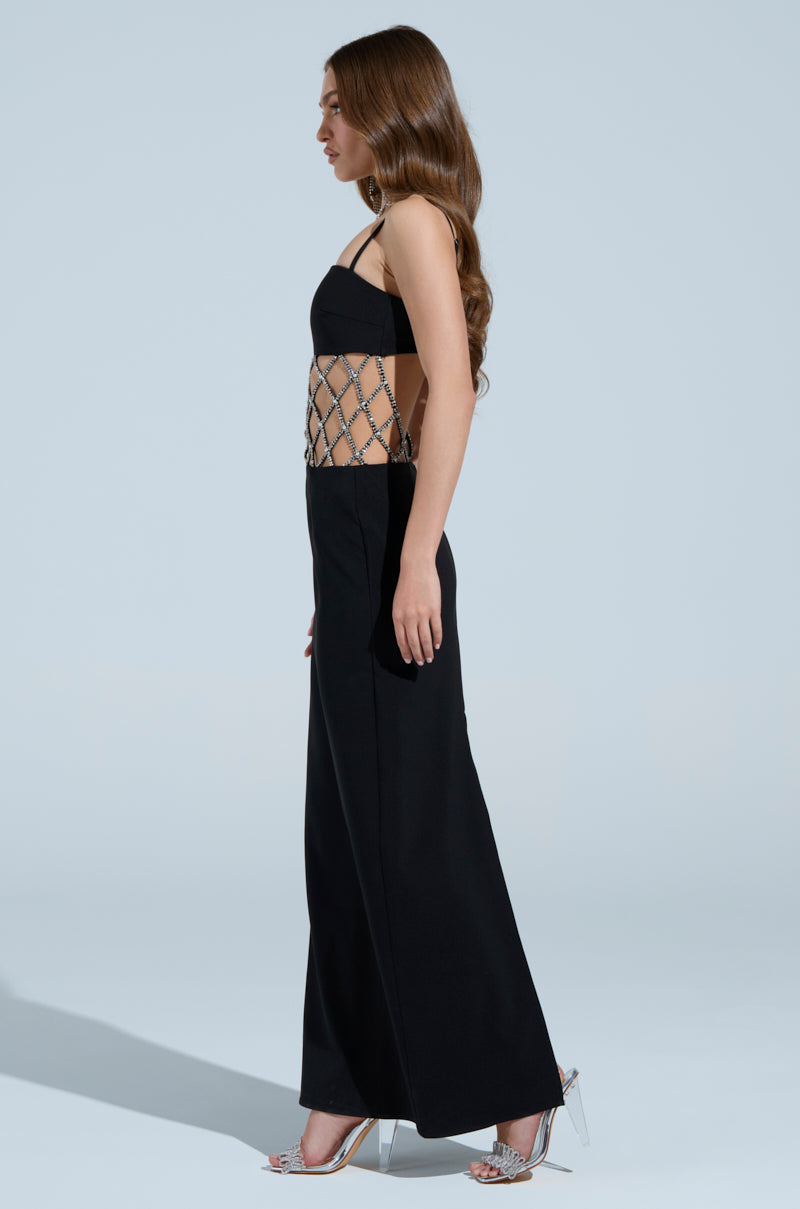 Side view of a woman with long hair wearing the "TAKE IT BLACK MIDI DRESS WITH RHINESTONE CUTOUT," featuring a black strapless design and semi-transparent midsection, paired with sparkling high heels against a plain light blue background.