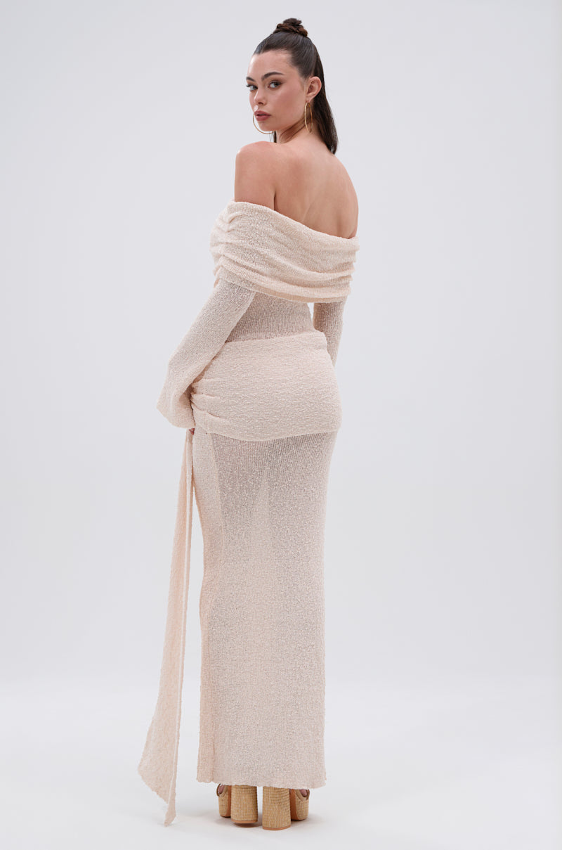 A woman models the IN YOUR DREAMS KNIT MAXI DRESS, featuring a textured, off-the-shoulder design, long sleeves, and a fitted silhouette, paired with high platform shoes against a plain light background.