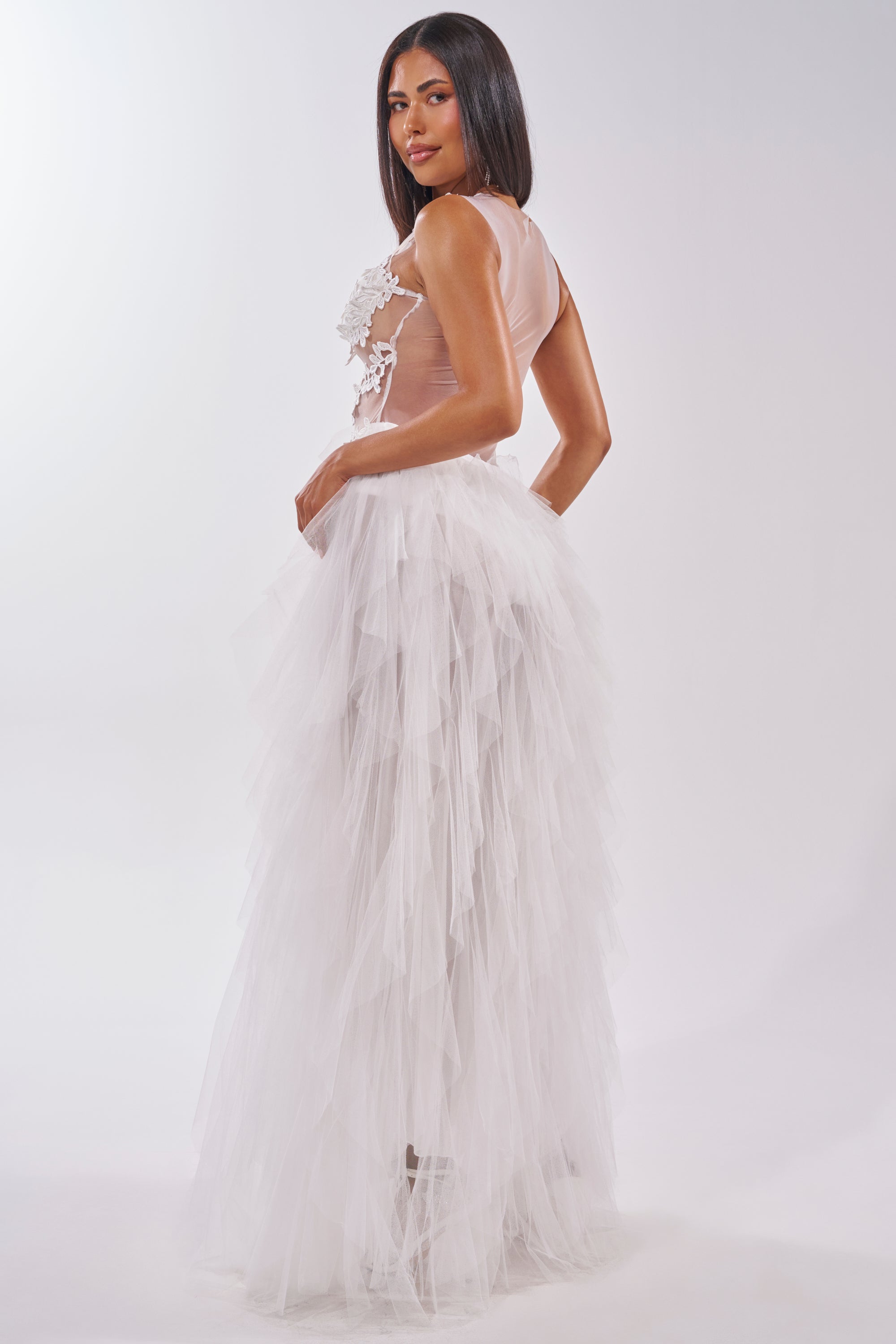 A woman poses in profile against a light background, wearing the FELT CUTE RUFFLE MAXI DRESS WITH FLORAL APPLIQUES, featuring sheer mesh with floral details and a layered white tulle skirt. She has straight dark hair. 4