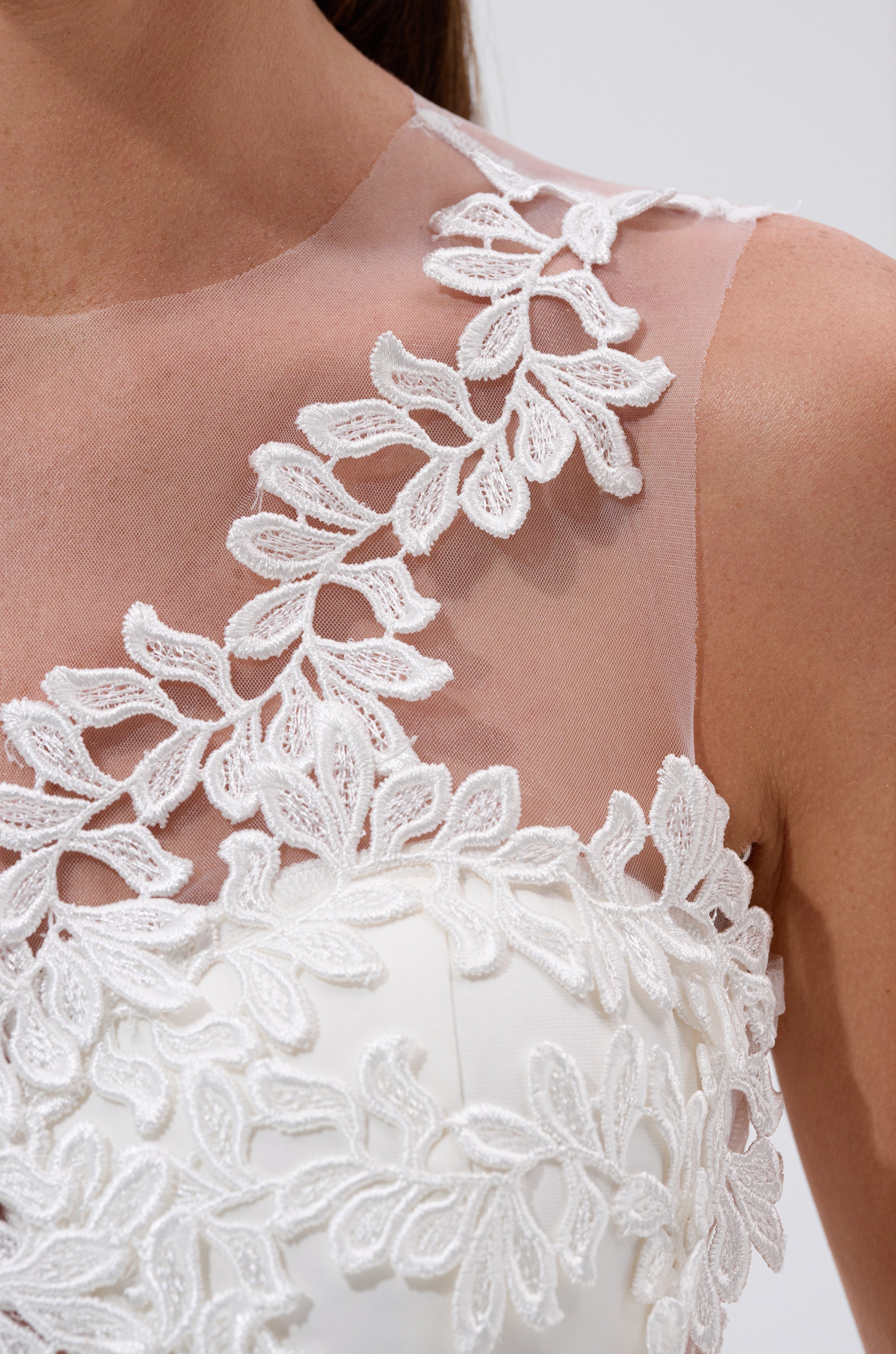 Close-up of the FELT CUTE RUFFLE MAXI DRESS WITH FLORAL APPLIQUES, showcasing its white fabric, intricate floral appliques, sheer mesh neckline, and scalloped lace edging on the shoulder and chest area.