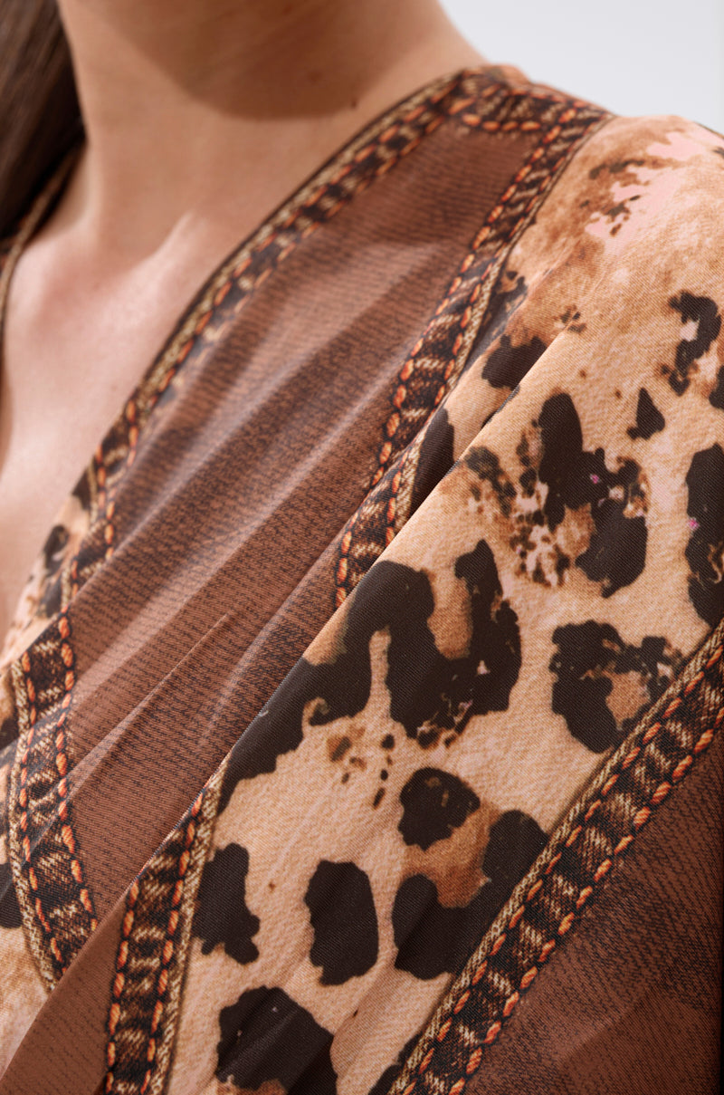Close-up of a person wearing the LOTS OF LOVE TO GIVE MIDI DRESS, featuring leopard patchwork and decorative edge stitching. Only the neckline, shoulder, and part of the chest are visible in this striking design.