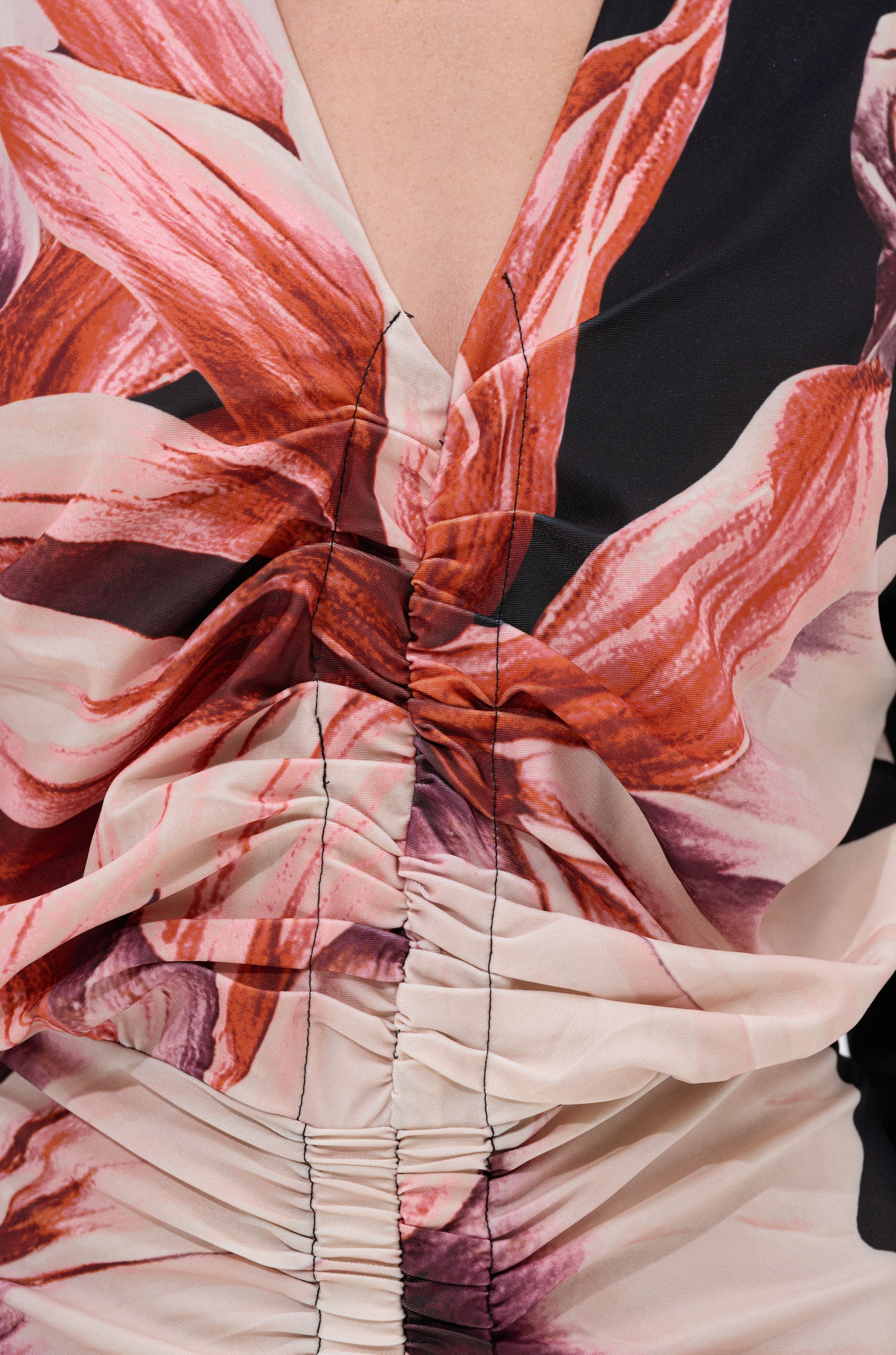 Close-up of the FLORAL BABY MIDI DRESS, featuring a deep V-neck, ruched fabric, and a vibrant pink, red, and cream floral print. Black stitching along the gathered center seam highlights its figure-flattering design. 4