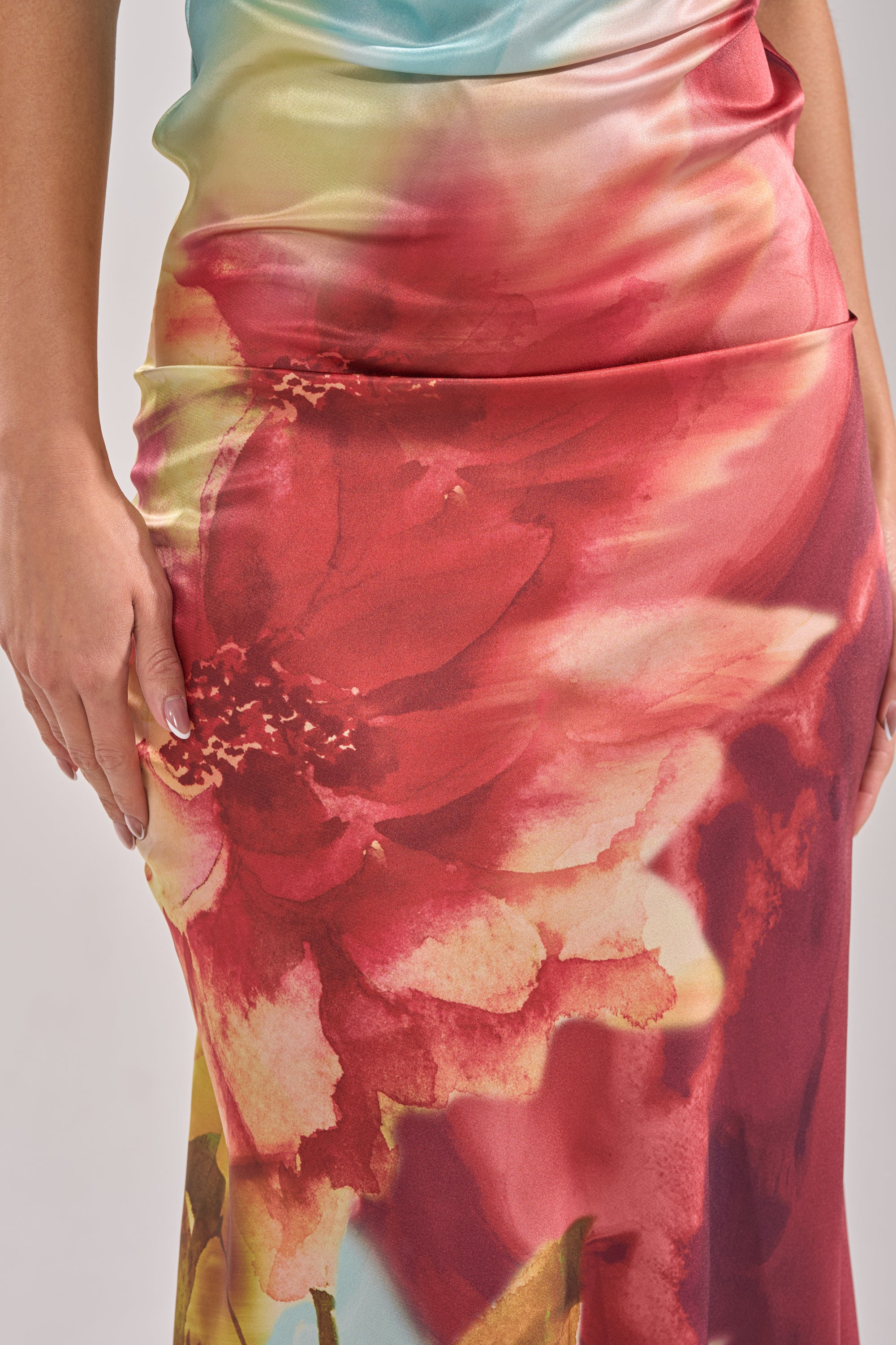 A close-up of a woman's hand resting on the WORK OF ART SATIN MAXI DRESS, highlighting its smooth satin texture and bold, colorful floral print. 11
