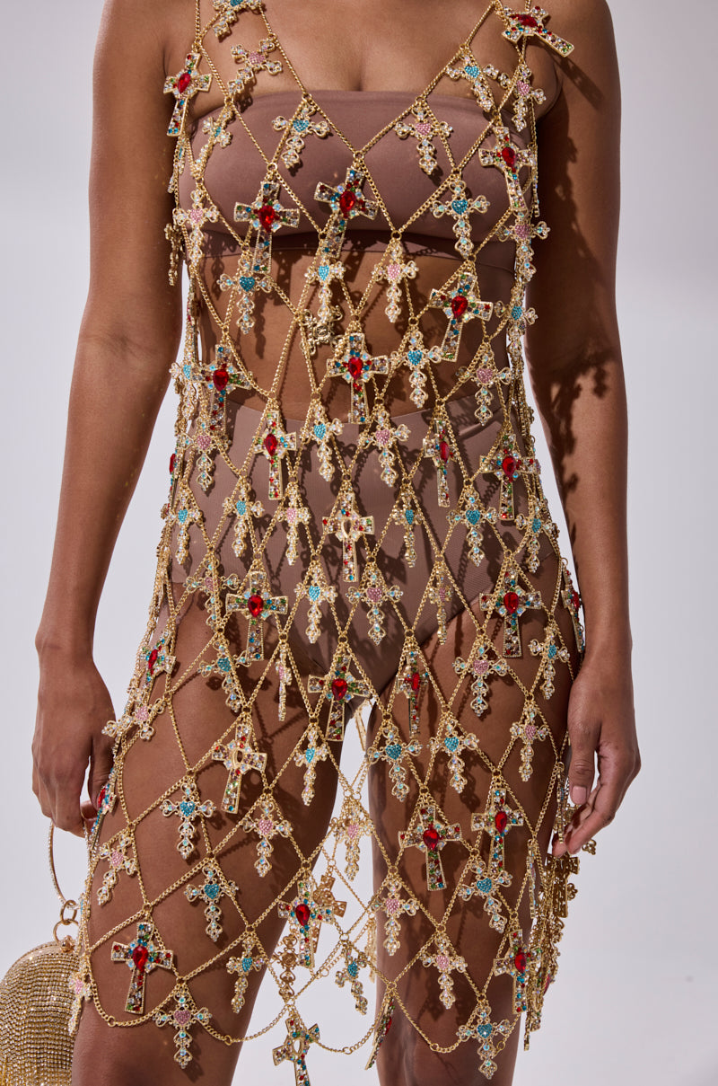 A person wears the EVE CROSS CHAIN MINI DRESS, a gold chain mini dress with rhinestone cross pendants and colorful jeweled crosses in a net pattern. The image is cropped from shoulders to thighs.