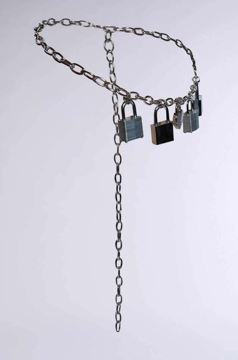 The HEART ON LOCK CHAIN BELT showcases large chain links with multiple silver padlock charms, displayed against a plain light background with one end of the chain hanging down. 2