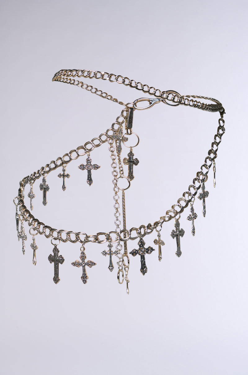 The ULTIMATE CROSS CHAIN BELT is festival-ready, featuring a silver chain with edgy hardware clips and small cross pendants. It boasts various chain links and circular connectors, crafting an intricate pattern against a plain background.