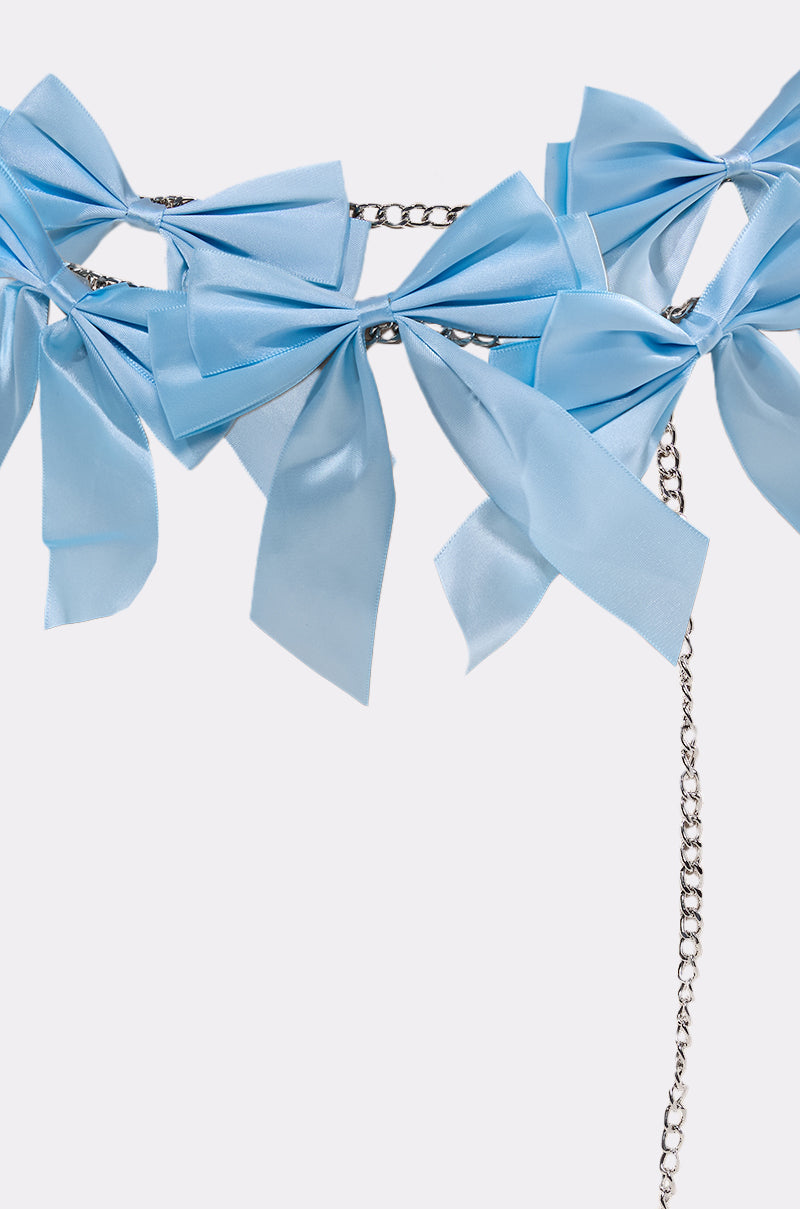 Close-up of the FEMME BOW BELT, a silver chain belt adorned with multiple large, shiny light blue satin bows, shown against a plain white background. 4